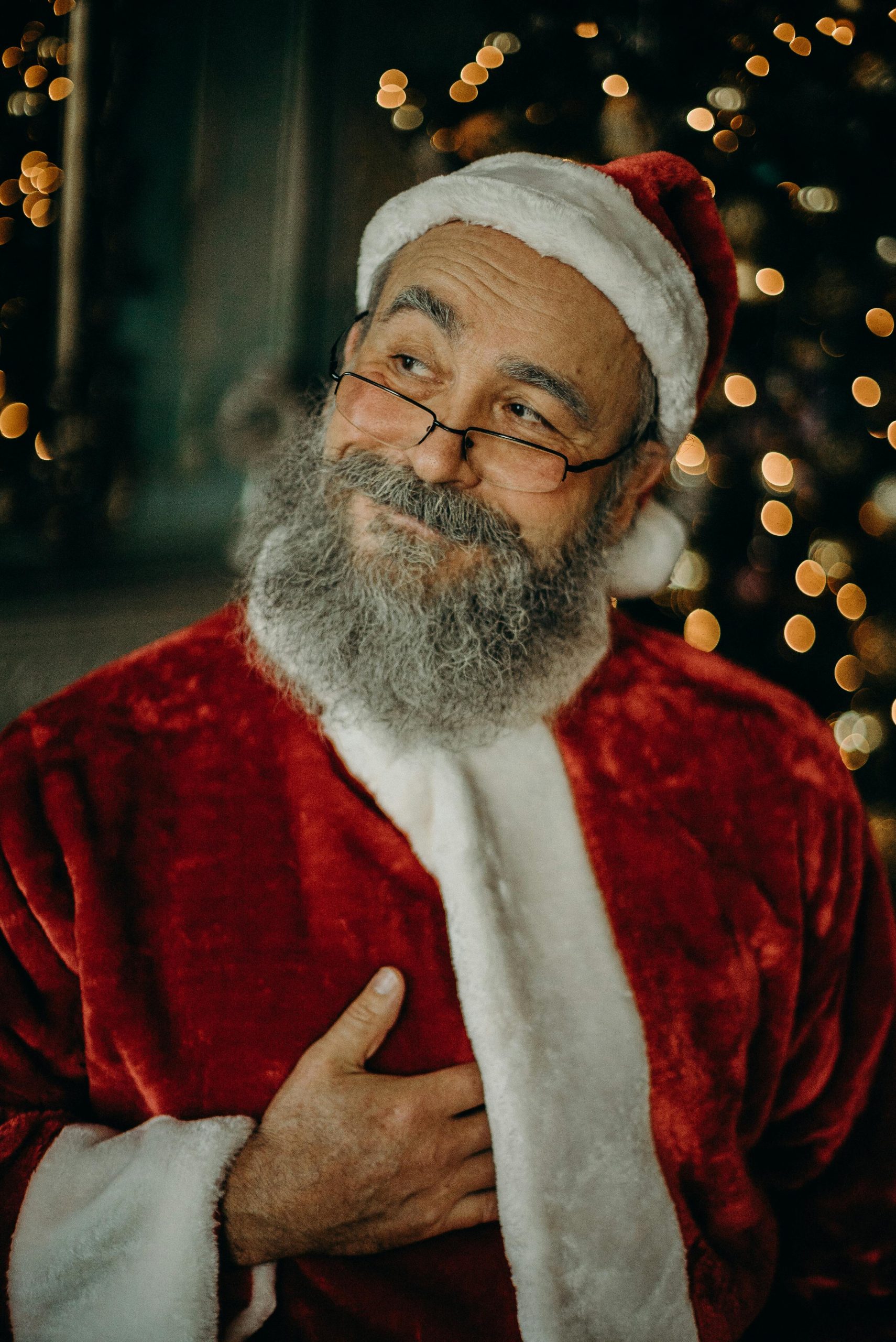 Charming portrait of a Santa Claus look-alike with twinkling lights in the background, captured indoors.